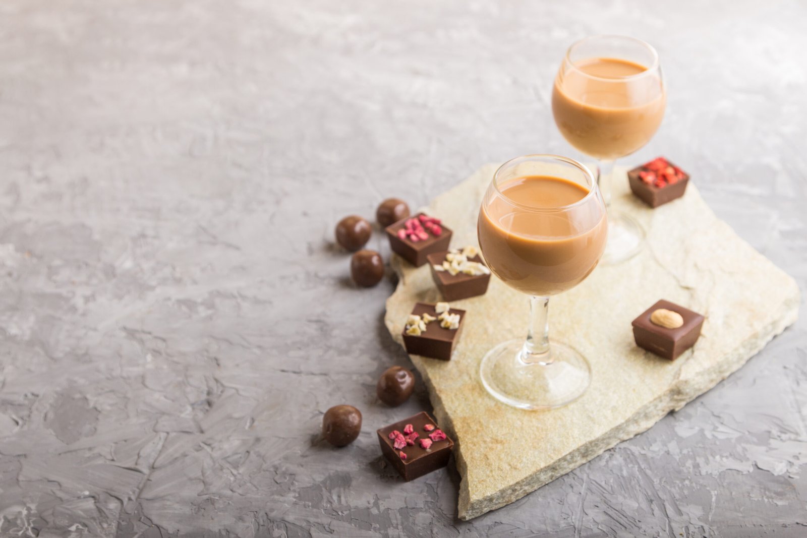 Sweet chocolate liqueur in glass on a gray concrete background a Sweet chocolate liqueur in glass with chocolate candies on a gray concrete background and stone slate board. Side view, copy space